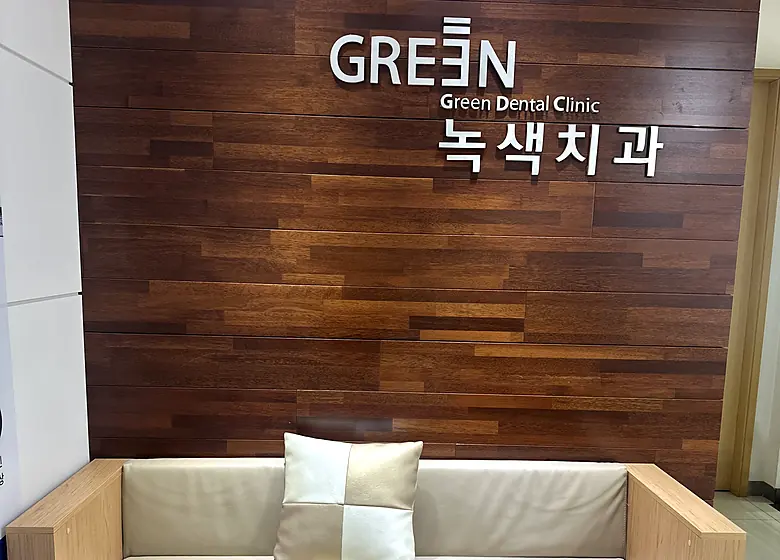 녹색치과의원 대기 공간 — 원목 벽면의 녹색치과 사인과 소파